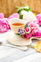 Cup of green tea and spring peonies blossom on a old wooden background with waffles and caramels. Rustic.