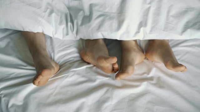 couple in bed. male and female legs from above, white linens. 4k