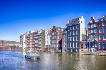 Naklejka premium People at Tourist Boat Attraction in Amsterdam at Damrak Canal With Boat Going to Pier in the Netherlands