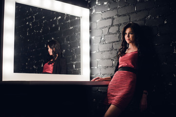 Sensual woman in a dark room. Modern loft interior, and stylish make up table with light bulbs.