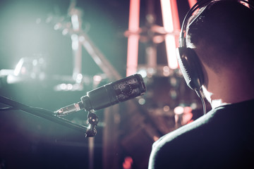 Person with headphones and Studio microphone close-up, in a recording Studio or concert hall, with a drum set.