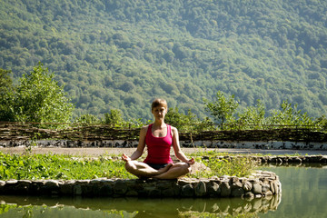 Fototapeta na wymiar girl in shorts and t-shirt meditating on the shore of a mountain lake sitting by the water