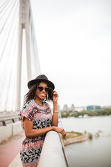 Young african american woman with hat poses while standing next to bridge fence