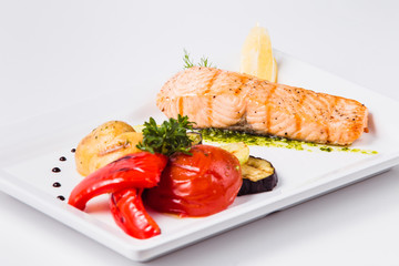 Healthy food, red fish, vegetables, herbs, lemon on a white plate and a white background
