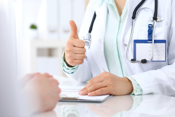 Doctor showing Ok sign  and thumb up to patient while sitting at the desk in hospital office, closeup of human hands. Medicine and health care concept