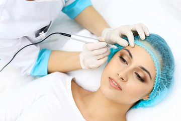 Fototapeta na wymiar Professional beautician doing eyebrow tattoo at woman face. Permanent brow makeup in beauty salon, closeup. Cosmetology treatment