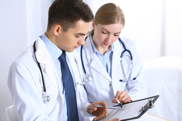 Doctors writing papers using clipboard. Physicians discussing medication program or studying at...