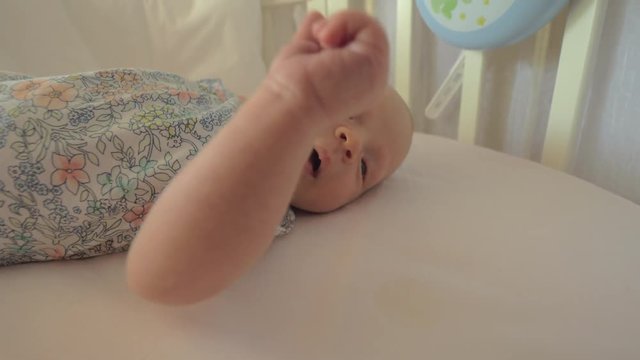 Awake newborn baby girl lying in crib at home. Child moving arms and yawning