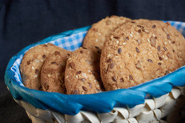 homemade oat cookies with sunflower seeds in and near blue checkered basket on black background