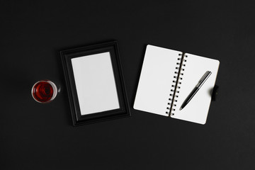 Glass of wine, photo frame and notebook on black background.