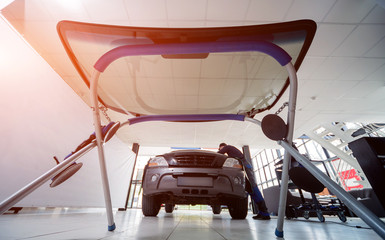 Automobile special workers replacing windscreen or windshield of a car in auto service station...