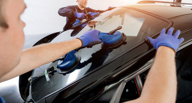 Automobile special workers replacing windscreen or windshield of a car in auto service station garage.