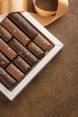 Handmade chocolate candies with golden splashes in box on wooden background