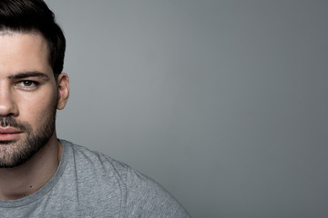 Close-up half of face of young bristled guy is standing and looking at camera confidently. Isolated background and copy space in the right side