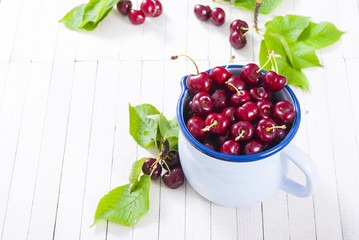 Cherry in old enamel mug, white wood table background