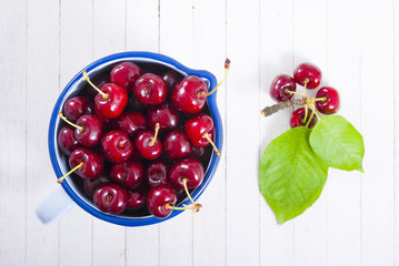 Cherry in old enamel mug, white wood table background