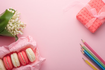 Flatlay macaroons, flowers and a gift and multicolored pencils with an empty place for inscription on a light pink background. Can be used as a postcard for a holiday