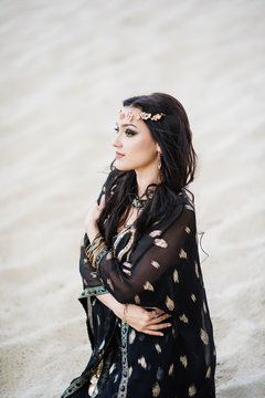 Dancer bellydance and Khaleegy (Khaliji) in a black suit in the desert against the background of sand. Image of Persian Gulf. Beautiful nature. Belly dance. A girl with an exotic look. Eastern beauty.