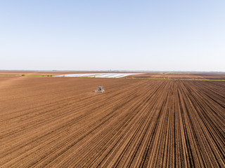 Aerial shot of a farmer seeding, sowing crops at field. Sowing is the process of planting seeds in the ground as part of the early spring time agricultural activities.