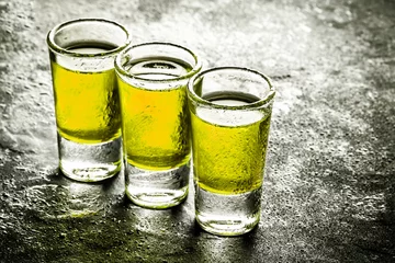 Crédence de cuisine en verre imprimé Bar Abstract yellow alcohol in wet vodka shots on black bar surface.