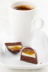 Cut handmade bonbon with ganache and fruit confiture filling with cup of coffee