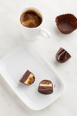 Top view of cut handmade bonbon with ganache and fruit confiture filling on plate with cup of coffee