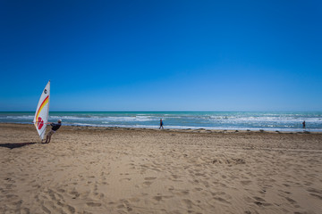 People walking on a beach on a sunny day and man preparing windsurfing, Bibione beach, Venice, Italy