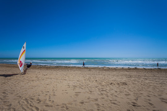 People walking on a beach on a sunny day and man preparing windsurfing, Bibione beach, Venice, Italy - Powered by Adobe