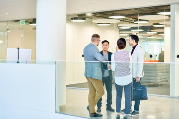 Full length portrait of group of young business people standing in circle in modern office building discussing project, copy space