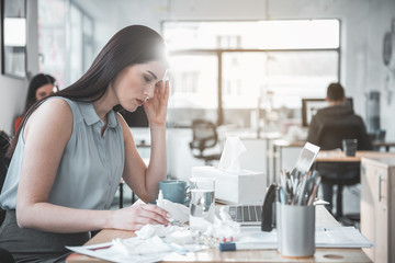 Side view sad sick female looking at digital device while sitting at table in office. Diseased employer at job concept