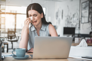 Portrait of crying lady wiping tears away tears with tissue paper while locating at desk with...