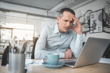 Portrait of depressed male having headache while watching at notebook computer. Frustrated employer...