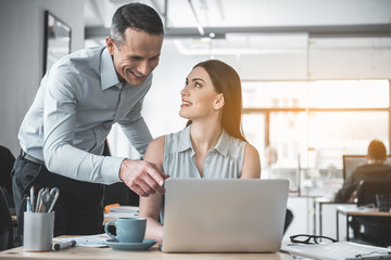 Outgoing female partner looking at glad man while typing in gadget. They talking during job. Friendly professional communication concept