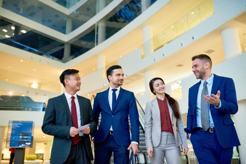 Group of cheerful young business people smiling happily while chatting on their way leaving modern office building