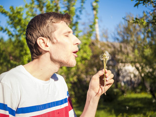 bearded man blowing at dandelion on a sunny day