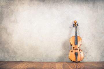 Vintage antique violin near old textured concrete wall background. Retro style filtered photo