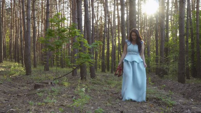 Beautiful woman in long blue dress walks in summer forest