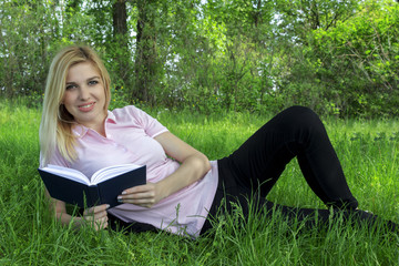 girl with a book lying on the grass, looking straight and smiling