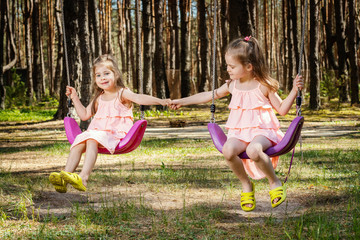 two little girls in dresses are playing on the swings in the park