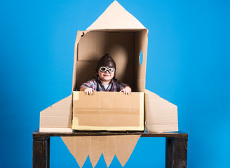 Kid in helmet and pilot glasses sit in cardboard rocket. Childhood concept - happy boy play astronaut. Cosmonaut concept - child with hand made toy rocket playing and dreaming of becoming spacemen.