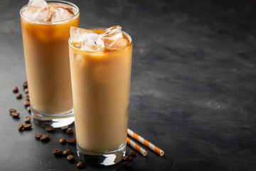 Ice coffee in a tall glass with cream poured over, brown sugar and coffee beans. Cold summer drink on a dark background. With copy space