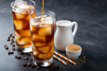 Ice coffee in a tall glass over and coffee beans on a old rustic wooden table. Cold summer drink on a dark background with copy space. The process of pouring drink from a coffee pot into a glass