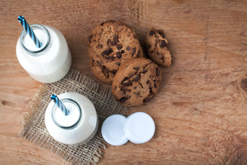 Two bottles of milk and chocolate chip cookies on dark background with copy space. Top view
