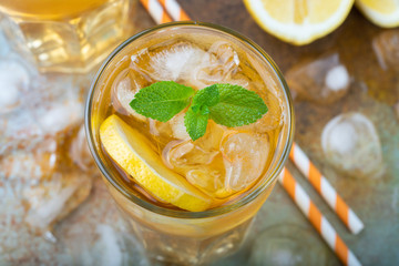 Traditional iced tea with lemon, mint and ice in tall glasses. A glass of refreshing summer drink on the old rusty background. Top view