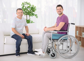 Mature man and his son in wheelchair indoors