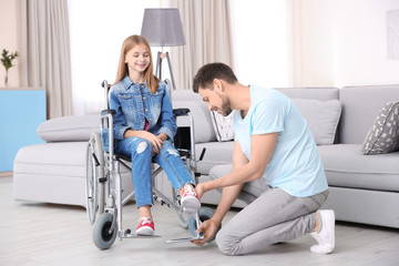 Young man taking care of teenage girl in wheelchair indoors