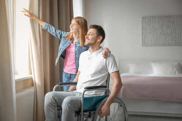 Young man in wheelchair and teenage girl near window indoors