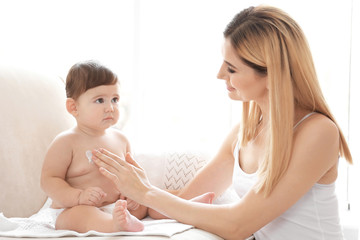 Obraz na płótnie Canvas Woman applying body cream on her baby indoors