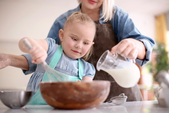 Little girl and her grandmother preparing dough together in kitchen