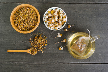 cup of chamomile tea with different size dried flowers on black wood table